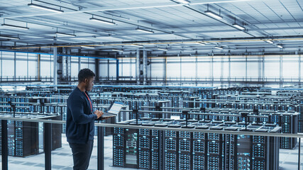 Data Center Engineer Using Laptop Computer. Server Farm Cloud Computing Specialist Facility with...