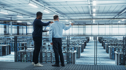 Male Data Center System Administrators and African American IT Specialists Talk, Use Laptop. Information Technology Engineers work on Cyber Security Network Protection in Cloud Computing Server Farm.