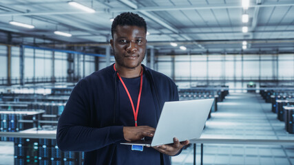 Portrait of a Data Center Engineer Using Laptop Computer. Server Room Specialist Facility with African American Male System Administrator Working with Data Protection Network for Cyber Security.