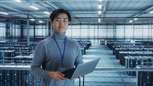 Portrait of a Data Center Engineer Using Laptop Computer. Server Room Specialist Facility with Korean Male System Administrator Working with Data Protection Network for Cyber Security. - Powered by Adobe