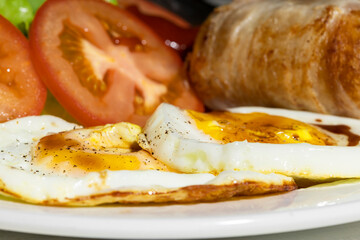 Close up fried eggs and sausages and tomato were placed on a white plate for breakfast.