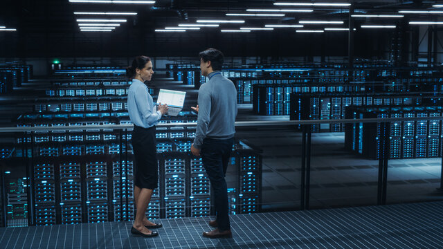 Data Center Female System Administrator and Male IT Specialist Talk, Use Laptop Computer. Information Technology Engineers work on Cyber Security Network Protection in Cloud Computing Server Farm. - Powered by Adobe