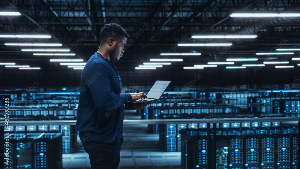 Poster Data Center Engineer Using Laptop Computer. Server Farm Cloud Computing Specialist Facility with African American Male System Administrator Working with Data Protection Network for Cyber Security.
