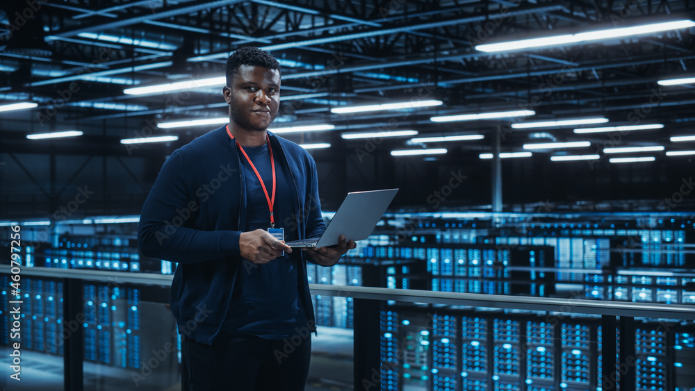 Aufkleber Portrait of a Data Center Engineer Using Laptop Computer. Server Room Specialist Facility with African American Male System Administrator Working with Data Protection Network for Cyber Security.