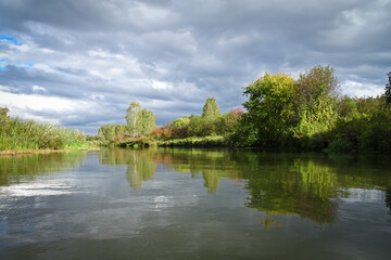 Summer landscape - calm river with smooth water surface under stormy sky with clouds.