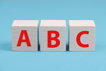 The letters A, B and C are standing on wooden cubes, blue colored background