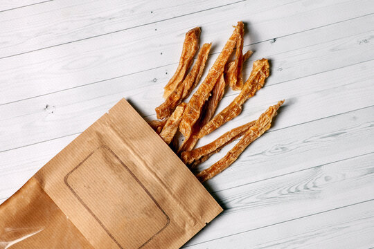 Sliced turkey or chicken meat dehydrated and packed into craft brown paper. Homemade natural dry dog treats. Wooden white background, empty place for logo, copy space.
