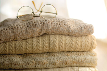 Pile of beige sweaters and retro eyeglasses. Selective focus.