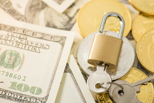 Closeup photo of golden padlock with inserted keys gold and silver coins with cryptocurrency symbols on hundred dollar bills
