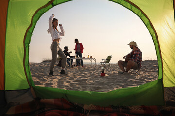 Friends resting on sandy beach, view from camping tent