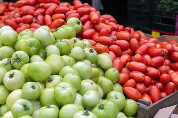 Close-up of piles of green and red tomatoes of different sizes in a wooden box on the market