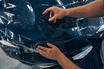 Closeup car service technician installs protective film with squeegee