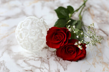 Glitter Christmas baubles and two red roses on a white marble surface. Luxurious and beautiful Christmas theme still life photo with red, white and glitter.