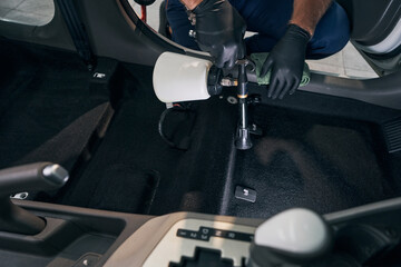Fototapeta na wymiar Man cleans interior of car service. Chemical washing of carpet textile