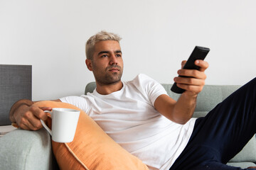Hispanic man channel-surfing while drinking a cup of coffee
