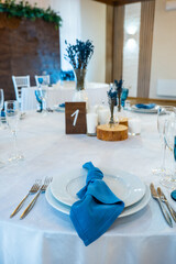 Detail of a wedding dinner setting. banquet table setting with blue napkins and glasses cutlery. vertical photo. table number one
