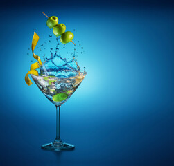 Martini glass with amazing splash as the result of olive berries falling down in it. Blue background.