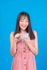 Beautiful Asian woman cute girl bangs hair style in red dress playing a smart phone isolated on blue background - mobile phone uses a online banking for pay online shopping