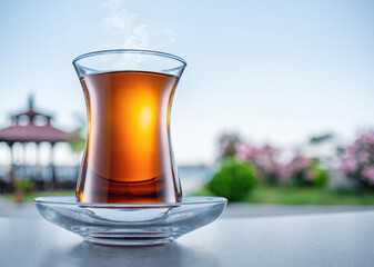 Turkish tea served in tulip-shaped glass on a small saucer blurred nature background. Summer holiday background.