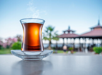 Turkish tea served in tulip-shaped glass on a small saucer blurred nature background. Summer holiday background.
