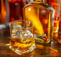 Whiskey decanter and glass of whiskey on the wooden bar counter close-up.