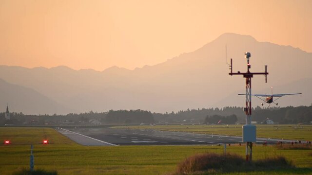 Small private ultralight plane landing against orange sky. Beautiful summer sunset at Ljubljana Airport, Slovenia. Small airplane with propeller engines descending on the runway. Real time, static