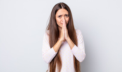 hispanic pretty woman feeling worried, hopeful and religious, praying faithfully with palms...