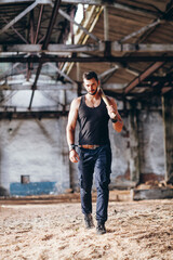 Strong Muscular Handsome Man in Black Tank Top with Baseball Bat Walksin Empty Grunge Hall
