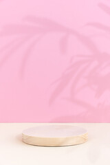 Minimal abstract background for the presentation of a cosmetic product. A cylindrical wooden scene on a beige table on a pink background. Premium podium with a shadow of tropical palm leaves on a pink