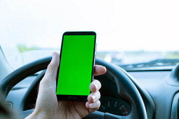 Mobile phone with a green screen in a man's hand inside a car. Blank screen for content integration, mock up