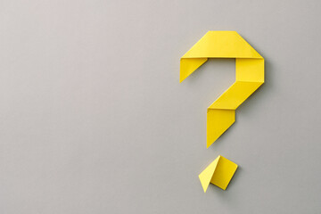 Decorative yellow paper origami question mark on grey