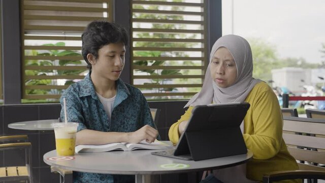A young teenage boy with an adult woman with hijab studying at a cafe