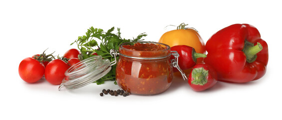 Glass jar of tasty adjika and ingredients on white background