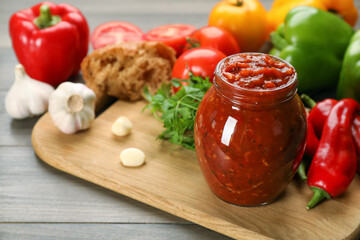 Glass jar of tasty adjika and ingredients on wooden table, space for text