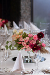 White tablecloths with clear vases and colourful flowers arrangements. Golden colored plates, peavh napkins, table numbers and mirror centerpieces.