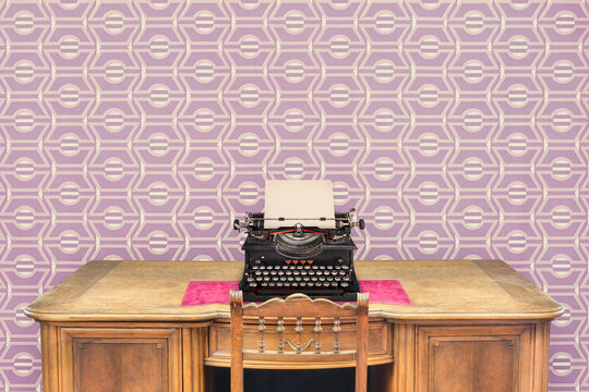 Ancient wooden desk with vintage typewriter in front of seventies purple wallpaper