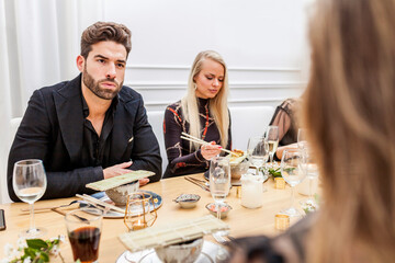 Group of friends conversating during dinner. Handsome man talking and eating sushi with female friends at a private dinner party. 