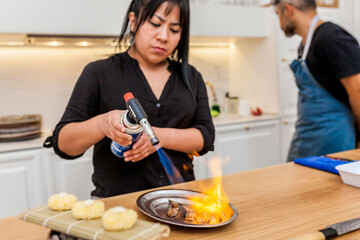 Latin cook preparing sushi with blowtorch at home. Cooking tuna with fire ignition. Luxurious dinner.