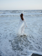 Fototapeta na wymiar Woman in white dress walks along the ocean coast landscape luxury