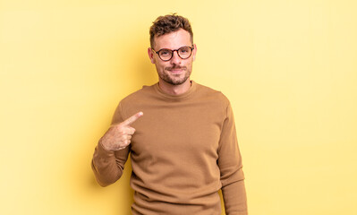 young handsome hispanic man looking proud, confident and happy, smiling and pointing to self or...