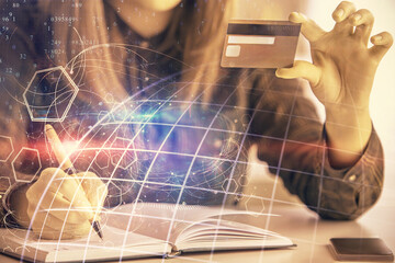 Double exposure of woman on-line shopping holding a credit card and world map hologram drawing. International E-commerce concept.