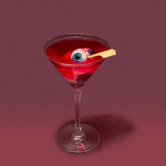 Devil awe drink concept. Martini glass full with eyeballs red color drink against mullberry purple background