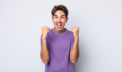 young handsome hispanic man feeling shocked, excited and happy, laughing and celebrating success,...