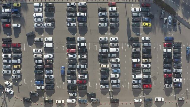 A lot of Cars moving around busy Parking lot near Big Shopping Center searching for a free parking place. 