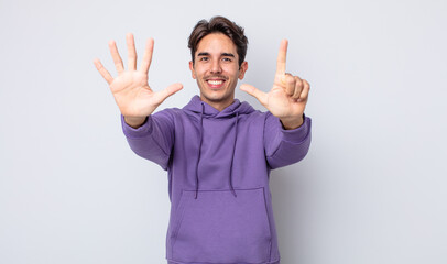 young handsome hispanic man smiling and looking friendly, showing number seven or seventh with hand...