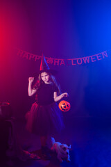 Funny child girl in witch costume for Halloween with pumpkin Jack and dog.
