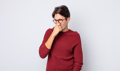 young handsome hispanic man feeling disgusted, holding nose to avoid smelling a foul and unpleasant...