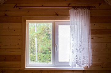 a window with a curtain and a pigeon on the windowsill in a new wooden house on the attic floor