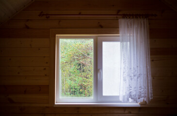 Fototapeta na wymiar a window with a curtain and a pigeon on the windowsill in a new wooden house on the attic floor