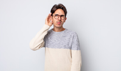 young handsome hispanic man looking serious and curious, listening, trying to hear a secret...